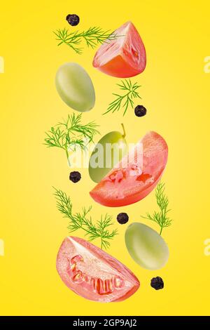 Isolated vegetables. Mixed tomatoes, dill, green olives and black pepper corns falling down isolate on illuminating colour with clipping path as packa Stock Photo