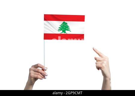 A beautiful female hand holds a Lebanon flag to which she shows the finger of her other hand, isolated on white background. Stock Photo