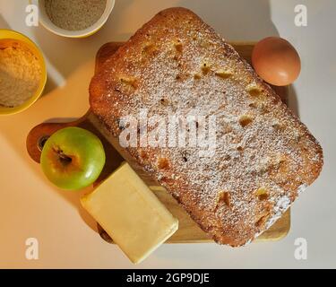 Apple Plum Cake decorated with an apple, an egg, butter, a cup of brown sugar and a cup of floor on a cutting table Stock Photo