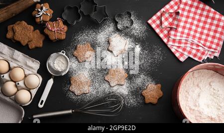 baked star-shaped gingerbread cookie sprinkled with powdered sugar on a black table and ingredients, top view Stock Photo