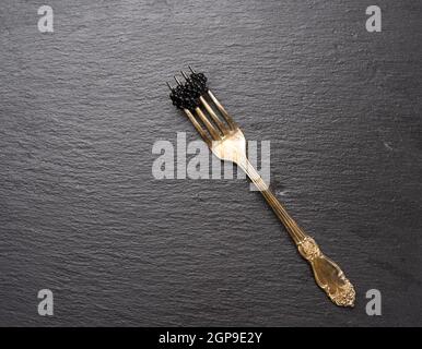 fresh grainy black paddlefish caviar in metal fork on a black background, top view Stock Photo