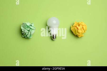 crumpled colored balls of paper and glass white lamp on green background, top view Stock Photo