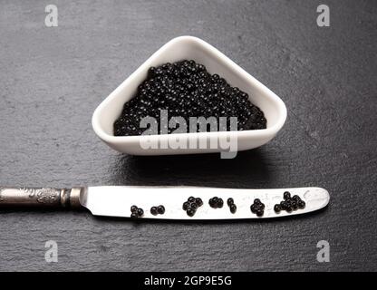 black grainy caviar of paddlefish fish in a white ceramic bowl, black background, top view Stock Photo