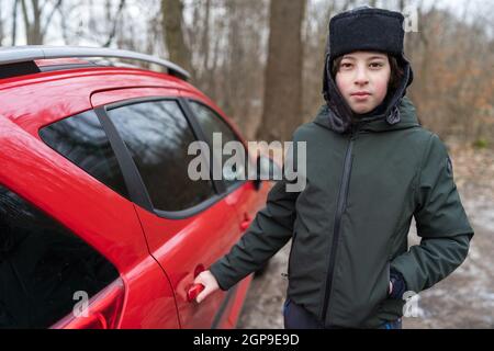 Portrait of a teenager in autumn clothes opens the passenger door of a car. Stock Photo