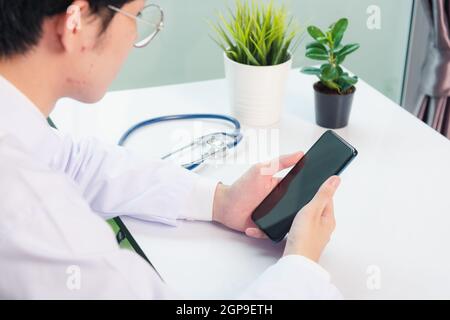 Asian doctor young handsome man smiling using working or holding with digital smart mobile phone at hospital desk office, Technology healthcare medica Stock Photo