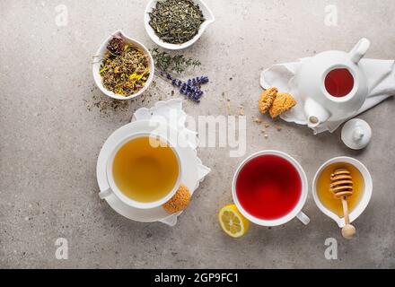 Herbal tea, green tea, fruit tea cups with honey and cookies on grey background Stock Photo