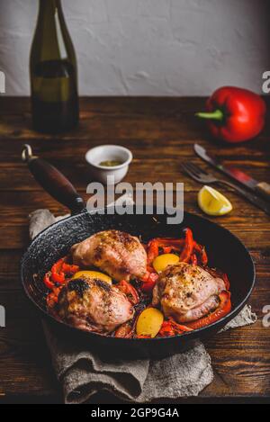 Chicken thighs baked with red bell peppers, rosemary and lemon in cast iron skillet. Stock Photo