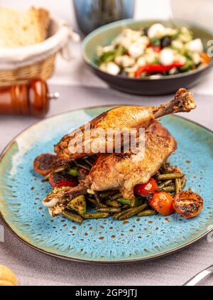 Duck leg confit with roasted vegetables served on the restaurant table Stock Photo