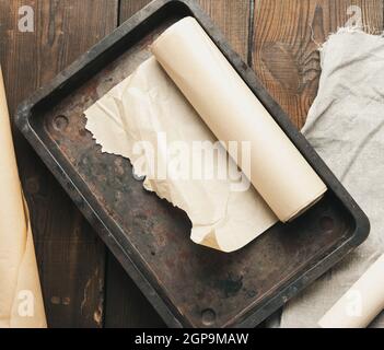 empty rectangular metal pan covered with brown parchment paper and paper rolls on a wooden table, top view Stock Photo