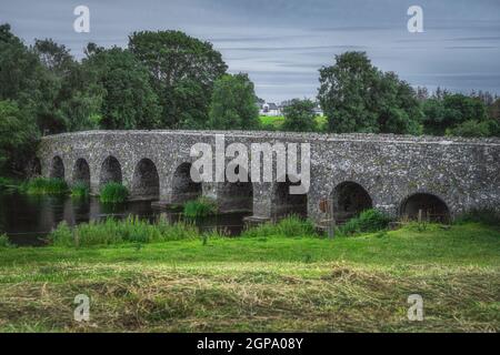 Closeup on old, 12th century stone arch Bective Bridge over Boyne River surrounded by green fields and forest, Count Meath, Ireland Stock Photo