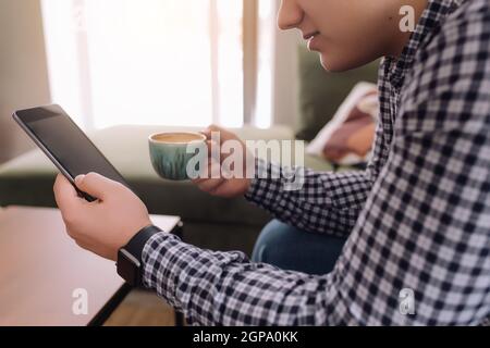 Smiling man holds and reading smartphone with black screen and coffee cup. Blurred background. High quality photo Stock Photo