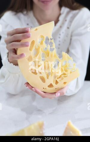 The girl holds large chunks of hard maasdam cheese. Cheese with lots of holes. Dutch Maasdamer cheese. An unrecognizable person.Chunks of cheese are o Stock Photo