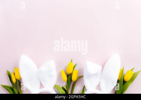 Easter concept. Flat lay with white fluffy rabbit ears, yellow tulips on a pink background. High quality photo Stock Photo