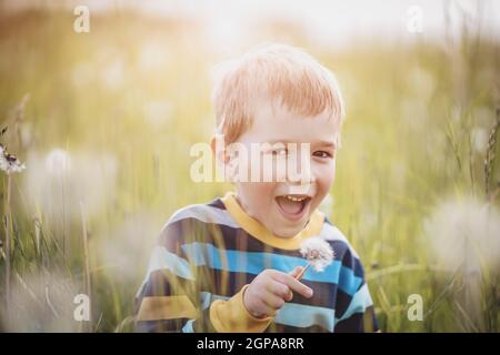 Happy boy standing on the field with dandelions Child outdoors in nature Stock Photo