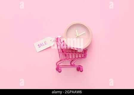 Alarm clock in small shopping cart on pink background, top view Stock Photo
