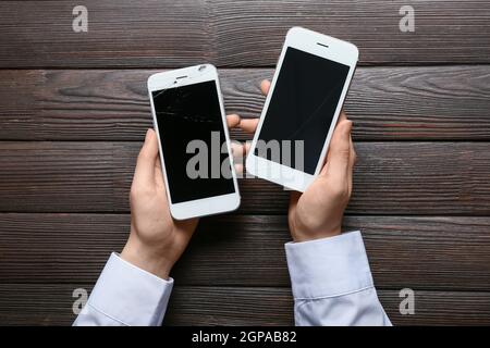 Woman holding broken mobile phones on wooden background