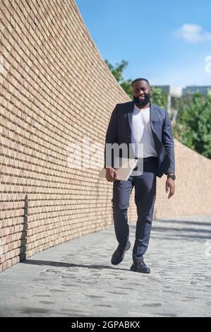 A dark-skinned man walking along the brick wall Stock Photo