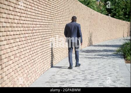 A dark-skinned man walking along the brick wall Stock Photo