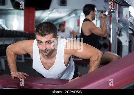 Man doing push-ups on bench in gym Stock Photo