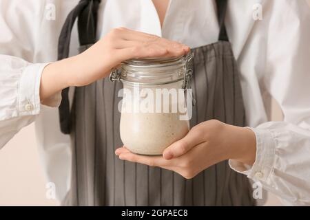 Woman holding glass jar of fresh sourdough on light background, closeup Stock Photo
