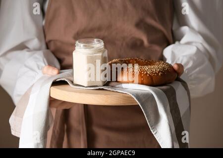 Woman holding wooden board with fresh sourdough and bagel on brown background Stock Photo