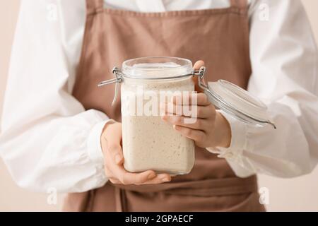 Woman holding glass jar of fresh sourdough on light background, closeup Stock Photo