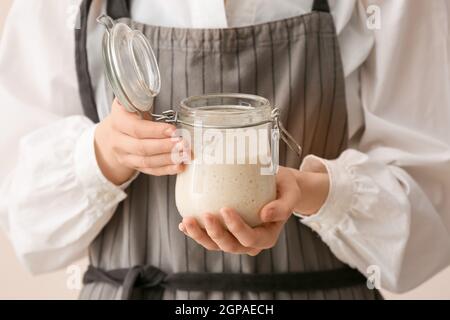 Woman holding glass jar of fresh sourdough on light background, closeup Stock Photo