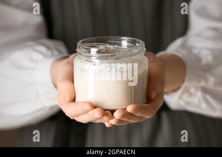 Woman holding glass jar of fresh sourdough, closeup Stock Photo
