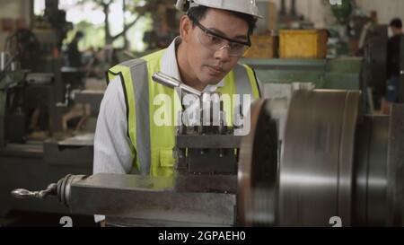 Asian professional mechanical engineer or operation man wear uniform goggles safety working on workshop metal lathe industrial manufacturing factory, Stock Photo