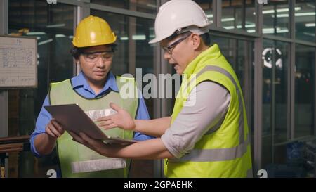 Two factory industrial workers technician or engineer and manager wear uniforms safety feeling upset with the engine machine of the factory arguing ab Stock Photo