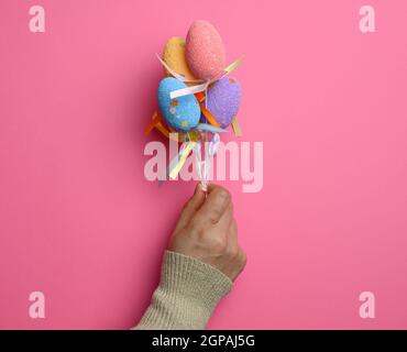 female hand holding multicolored decorative easter eggs on pink background, close up Stock Photo