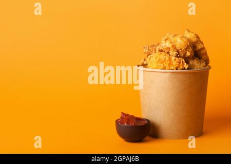 Paper bucket with tasty popcorn chicken and tomato sauce on color background Stock Photo