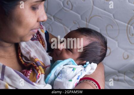 Close up face of a cute newborn baby boy happily looks at his mother in her mother lap. One month old Sweet little infant toddler. Indian ethnicity. F Stock Photo