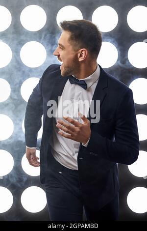 handsome man in tuxedo run against the backdrop of spotlights and smoke. night life Stock Photo