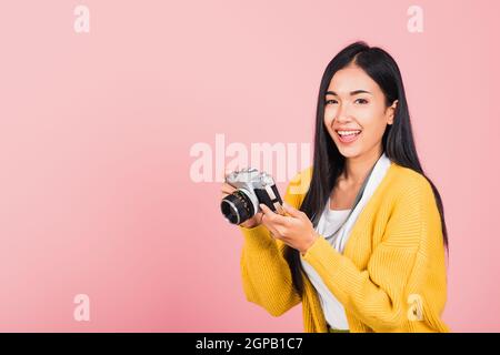 Attractive energetic happy Asian portrait beautiful cute young woman teen excited smiling holding vintage photo camera, studio shot isolated on pink b Stock Photo