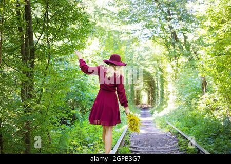 girl standing on the tracks in the woods with a bouquet of yellow flowers. Tunnel of love - Ukraine Stock Photo