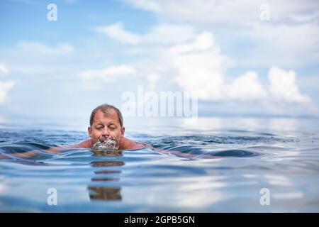Senior man swimming in the Sea/Ocean - enjoying active retirement, having fun, taking care of himself, staying fit Stock Photo