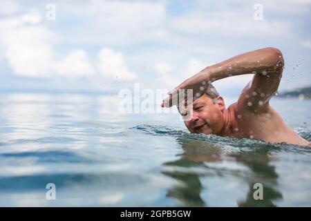 Senior man swimming in the Sea/Ocean - enjoying active retirement, having fun, taking care of himself, staying fit Stock Photo