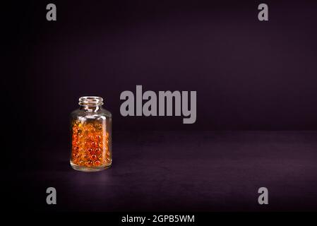 A glass jar with pills of bright orange yellow color on a lilac background. Place for the label, logo, layout. Stock Photo