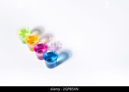 Plastic multi-colored glasses with liquid on a white background with highlights. Layout, mockup. Stock Photo