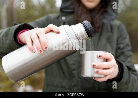 Youg beautifull women pouring beverage from termos to cup in a cold raini day. Healthy living and hiking. Stock Photo