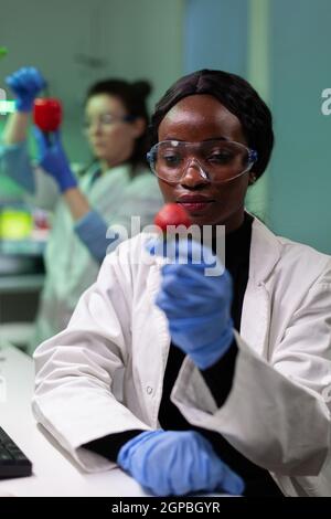 African american scientist holding organic strawberry examining modified genetically fruits during botany experiment. Biochemist working in biochemistry hospital laboratory testing gmo fruit Stock Photo