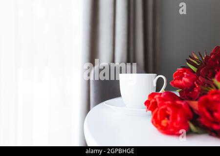 Red tulips bouquete on table, white coffee cup. Concept for greeting card for mothers day, international womans day or valentines day concept, birthda Stock Photo