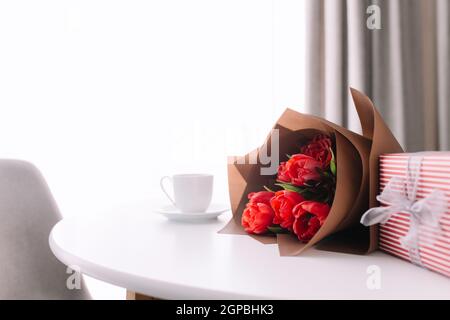 Red tulips bouquete on table, white coffee cup. Concept for greeting card for mothers day, international womans day or valentines day concept, birthda Stock Photo