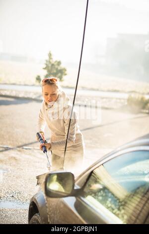 Pretty, young woman washing her car in a manual carwash (color toned image) Stock Photo