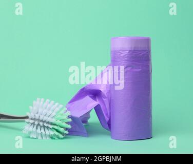 plastic brush and skein of purple plastic trash bags with strings on a green background, close up Stock Photo