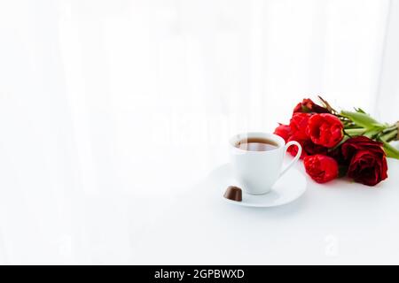 Red tulips bouquete on table, white coffee cup. Concept for greeting card for mothers day, international womans day or valentines day concept, birthda Stock Photo