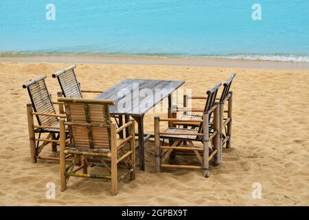 Wooden bamboo furniture, table and five chairs around on sand beach with blue sea water background in Koh Samui island, Thailand Stock Photo