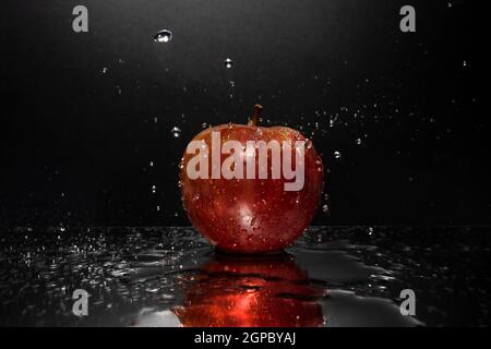 A red apple resting on a mirror with falling water drops Stock Photo