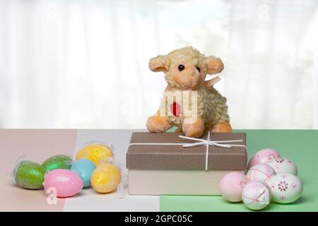 Happy Easter greeting card. Decorative composition of colorful eggs, a gift box with a easter lamb on it on a multicolour table in front of modern abs Stock Photo